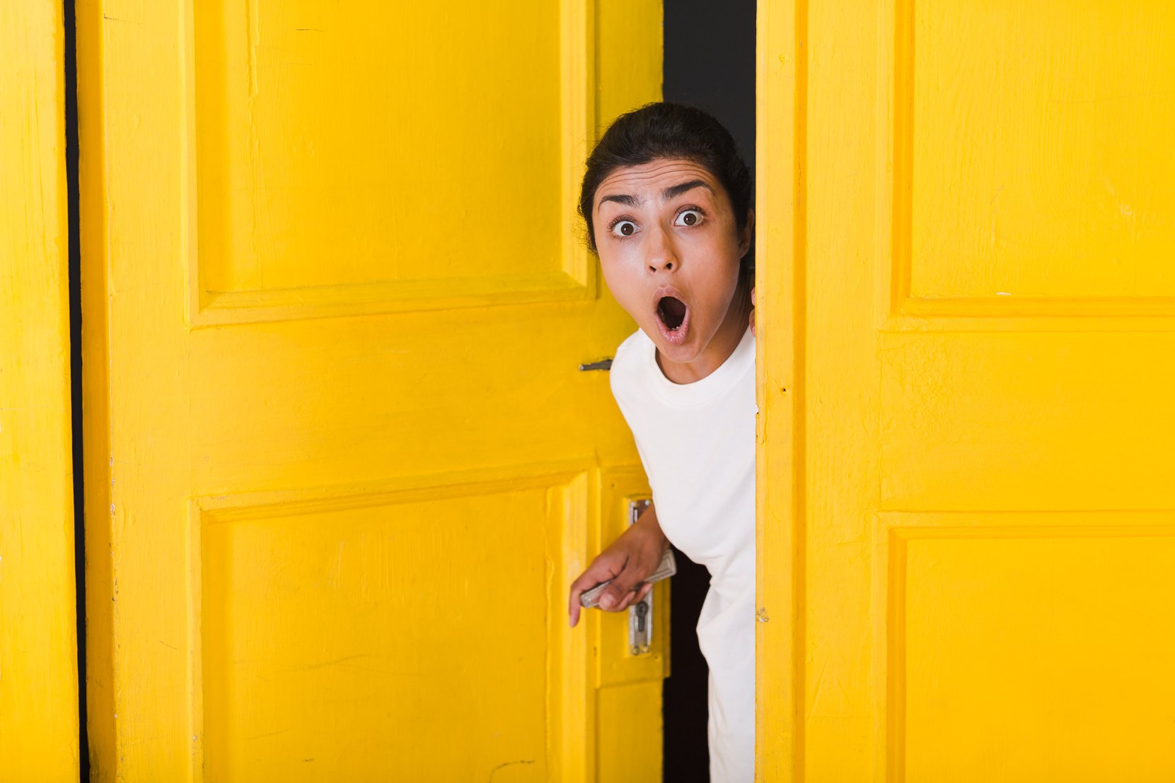 Young Indian Woman Peeking through Yellow Door.